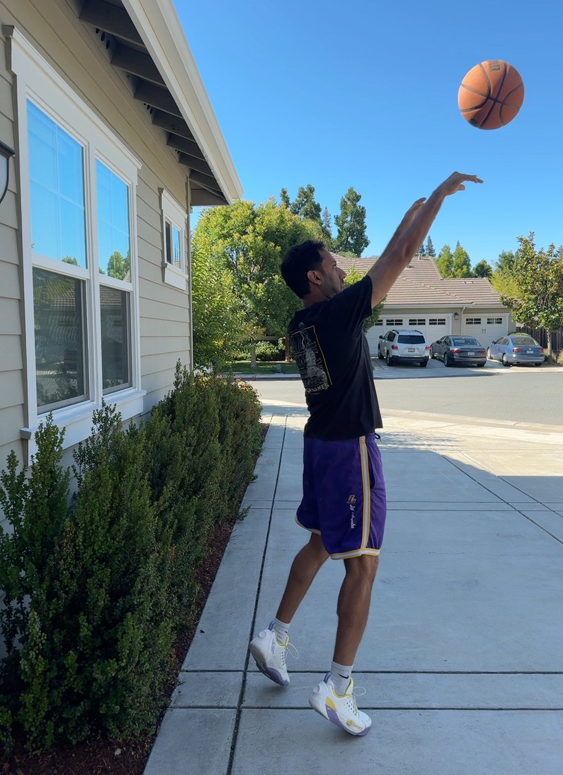 A shooter caught at full extension on a driveway, ball in the air just after release